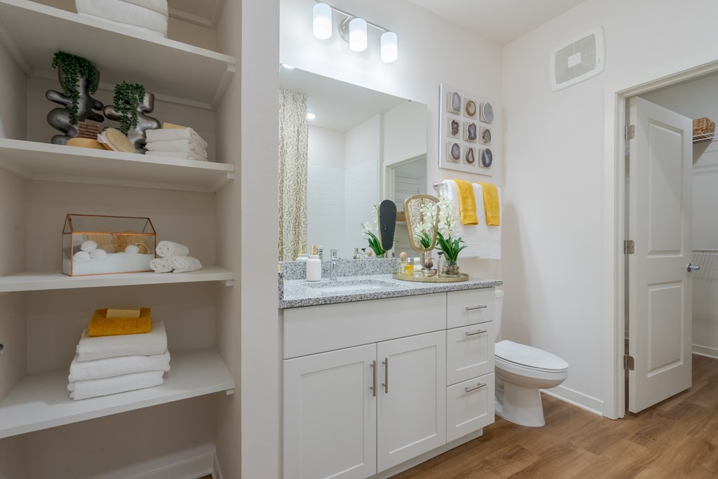 A white bathroom with a toilet, sink, and shelves with towels and plants.