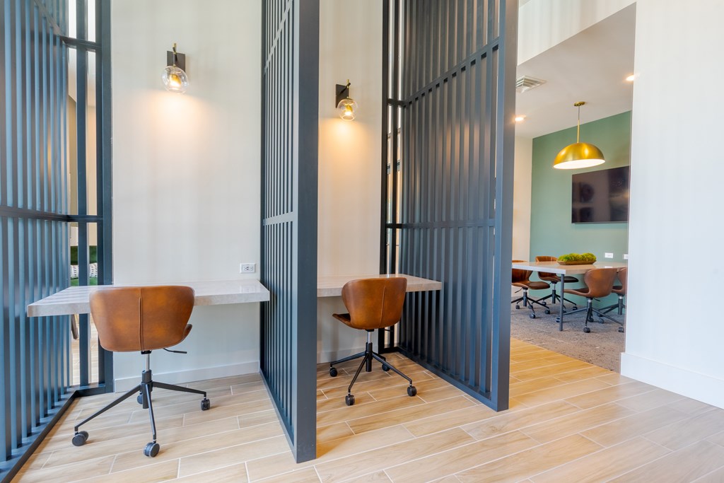 A room with a white desk and brown chairs with a grey partition.
