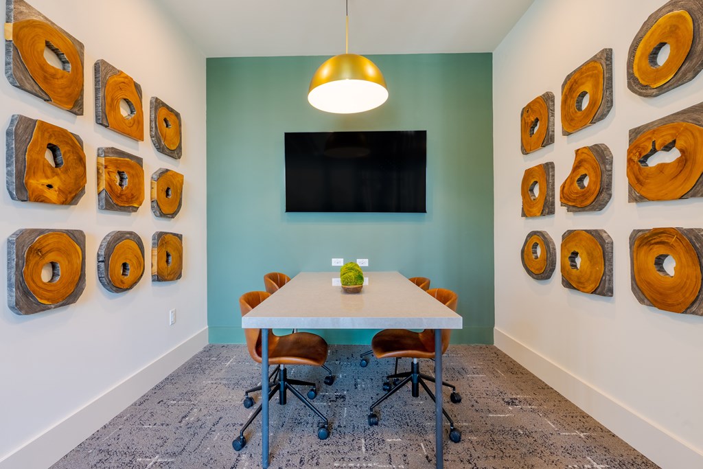 A conference room with a white table and chairs, a television, and a wall of wood slices.