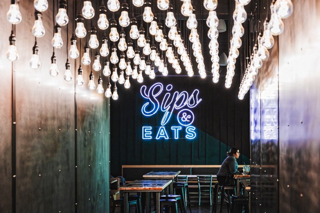 a man sitting at a table in a restaurant with a neon sign