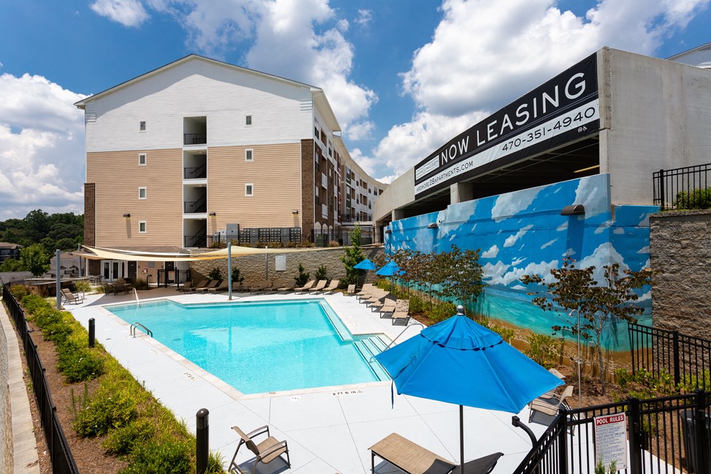 A pool with a blue umbrella and a building with a sign that says "Now Leasing".