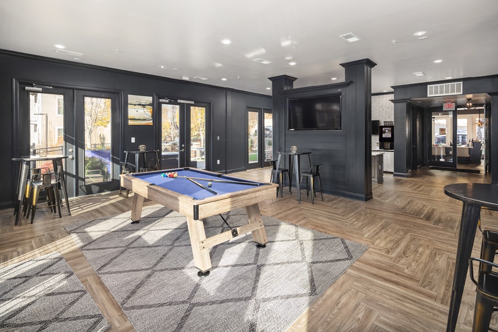 A pool table is in the middle of a room with a television and a bar.