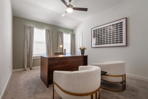A room with a desk, chairs, and a ceiling fan.
