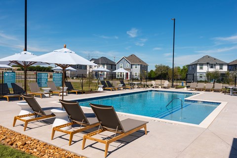 A pool with chairs and umbrellas in front of a row of houses.