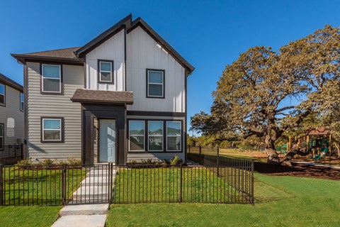 A modern house with a black fence and a tree in the front yard.