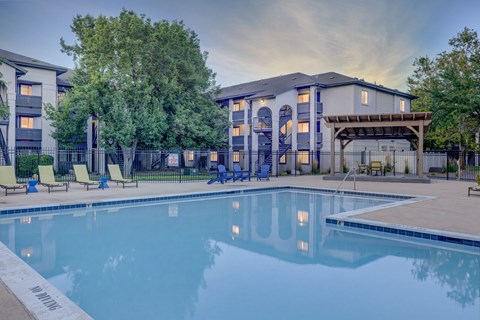 A swimming pool in front of a building with a patio area.