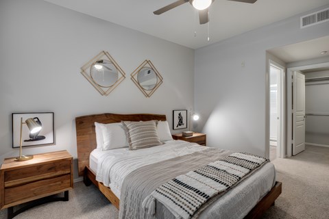 A bedroom with a bed, nightstand, and two mirrors on the wall.
