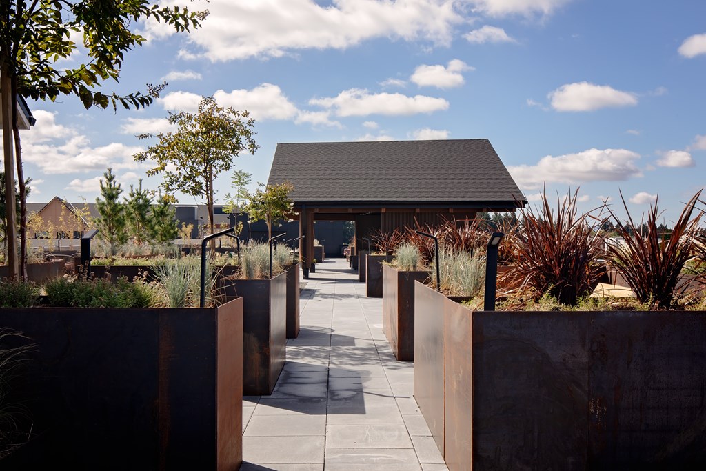 A modern building with a grey roof is surrounded by a metal fence and concrete planters.