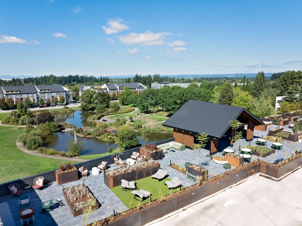 A large building with a black roof is surrounded by a garden and a pond.