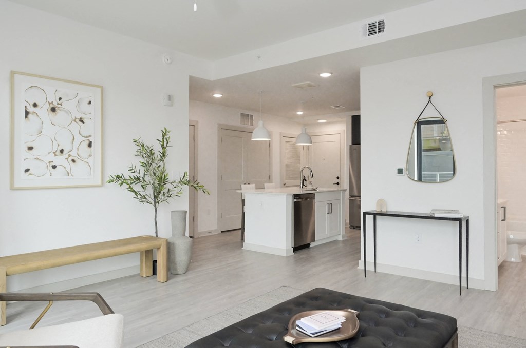 a white living room with a kitchen and a black ottoman