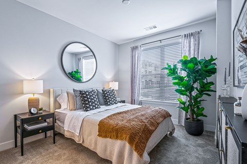 A bedroom with a bed, nightstand, and a plant.