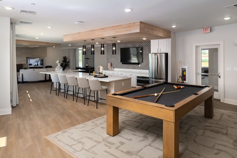 A pool table is in the middle of a room with a kitchen in the background.