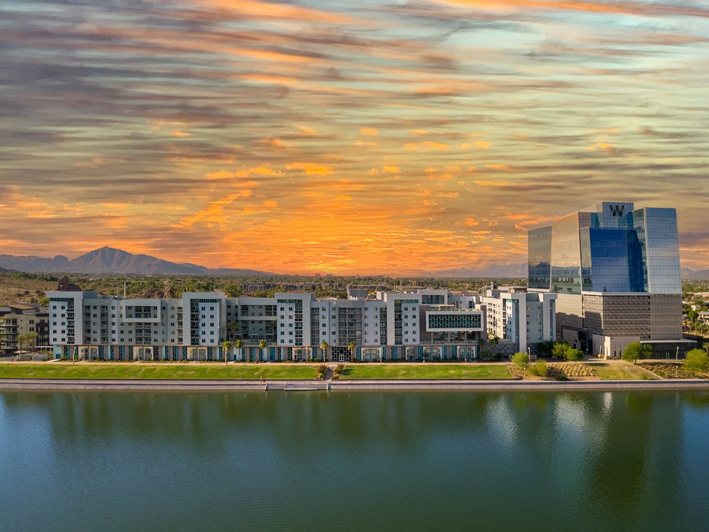 a cityscape with a lake in the foreground and a sunset in the background