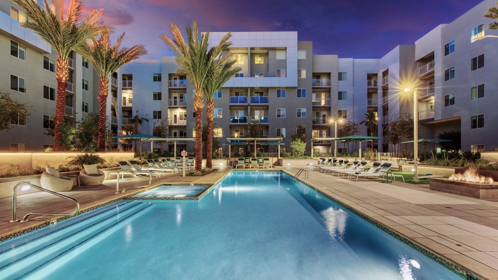A swimming pool is surrounded by palm trees and lounge chairs at a resort.
