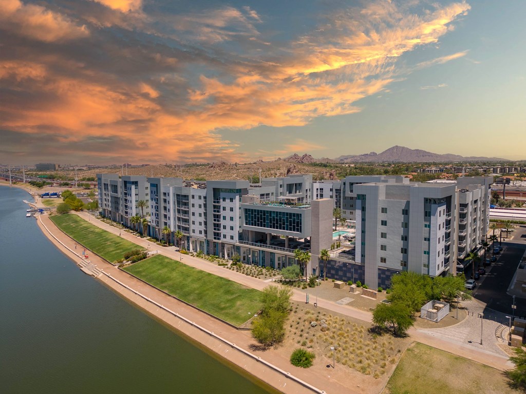 A modern apartment complex is situated along a riverbank with a mountain in the distance.