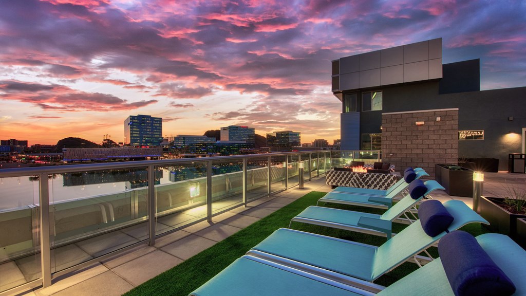 A modern building with a pool and lounge chairs is illuminated by the setting sun.