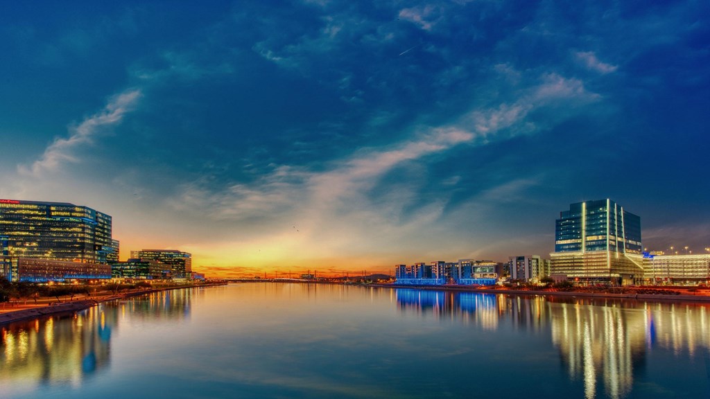 A cityscape at dusk with buildings reflecting in the water.