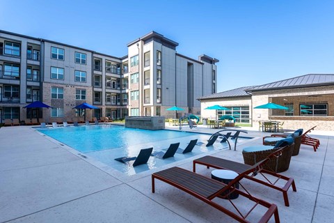 A swimming pool surrounded by lounge chairs and umbrellas in front of a building.