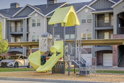 a playground with a yellow slide in front of an apartment building