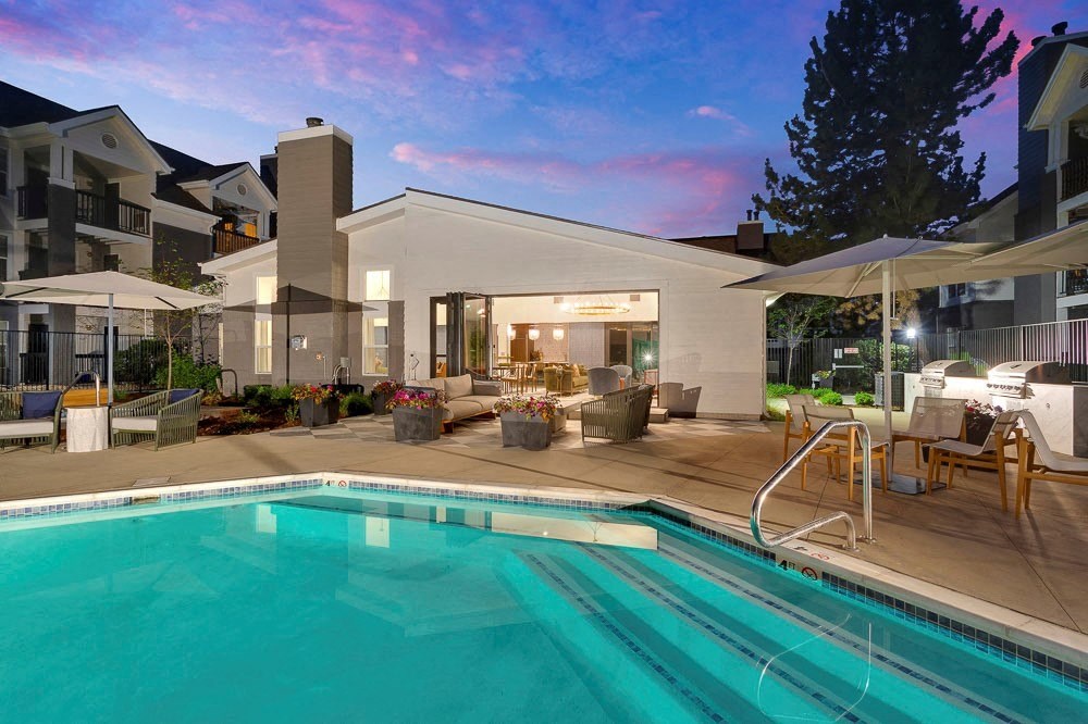 A swimming pool in front of a modern building with a sunset in the background.