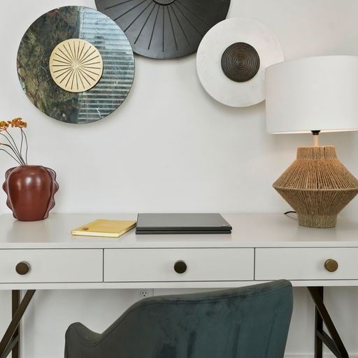 A white desk with a laptop, a vase, a notebook, and a lamp.