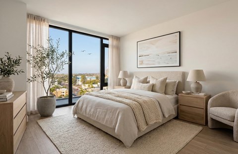A bedroom with a large bed, a chair, and a view of the outside through a large window.