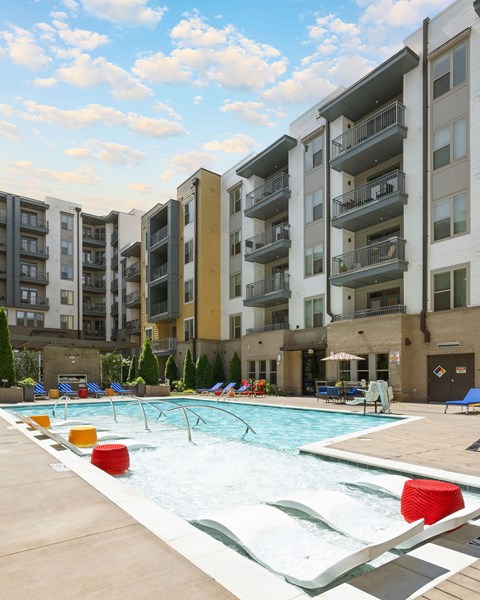 A large swimming pool with red and yellow lounge chairs in front of apartment buildings.