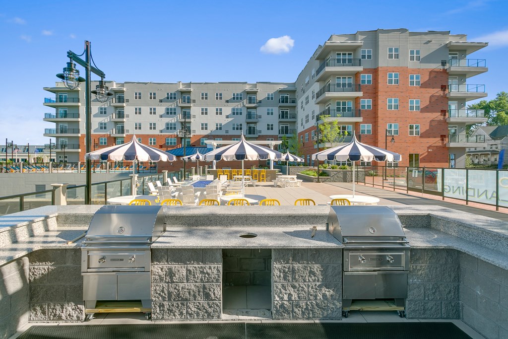 Outdoor grilling station overlooking patio with table seating and umbrellas