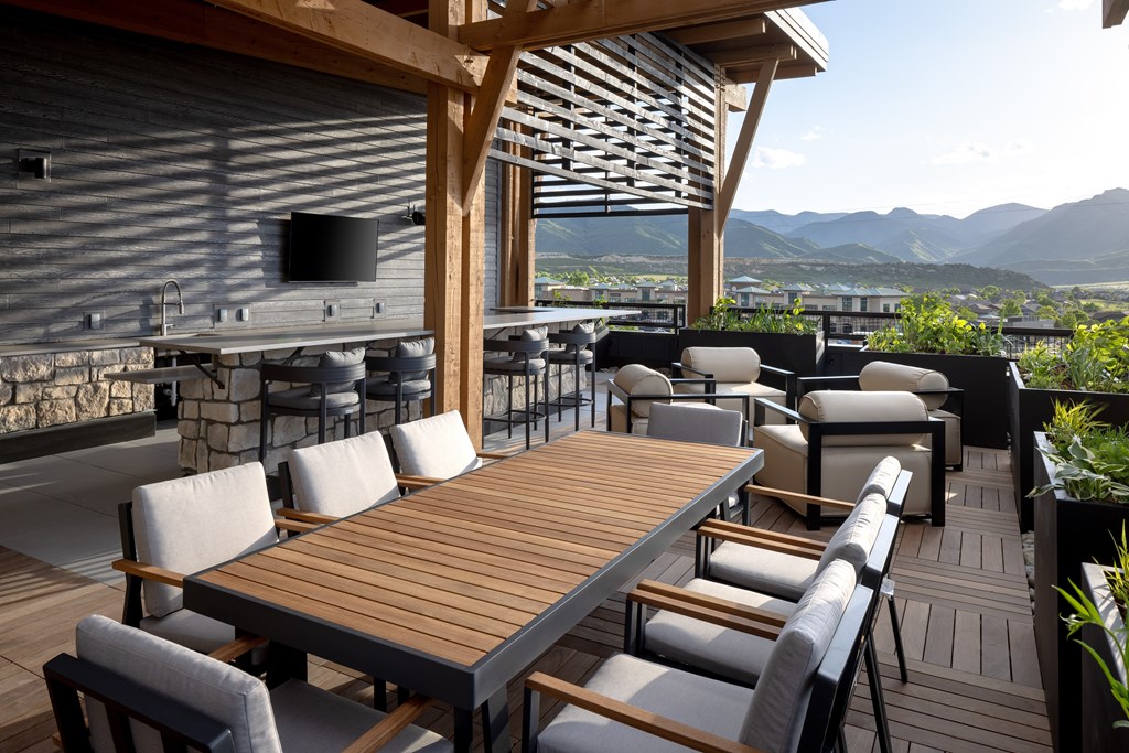 A wooden table and chairs are set up on a patio with a mountain view.