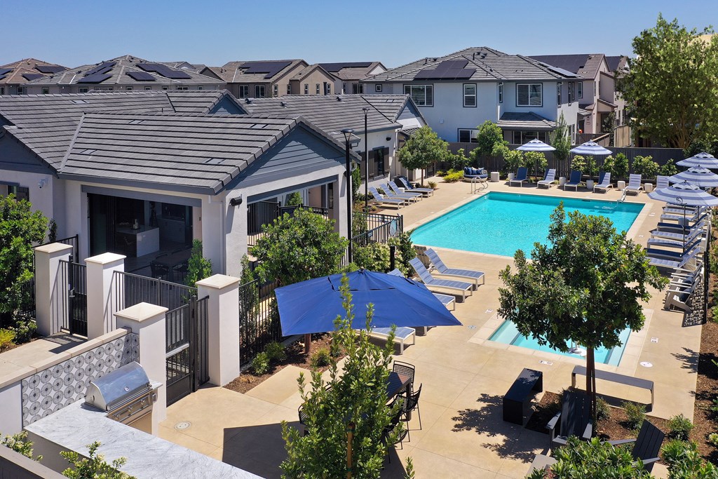 A pool surrounded by trees and chairs with a house in the background.