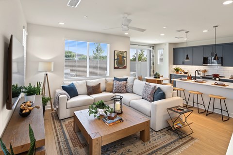 A modern living room with a white sofa, a wooden coffee table, and a kitchen area in the background.