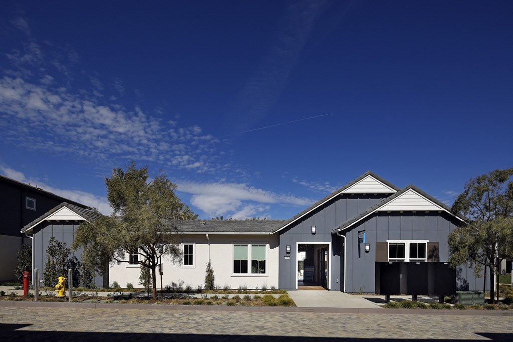 A modern building with a white and grey exterior is surrounded by a gravel driveway and a few trees.