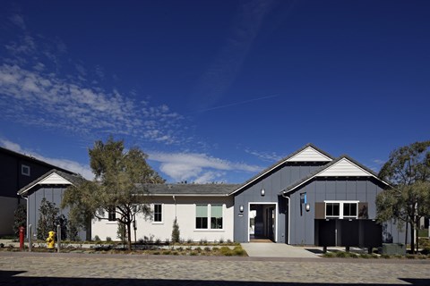 A modern building with a white and grey exterior is surrounded by a gravel driveway and a few trees.