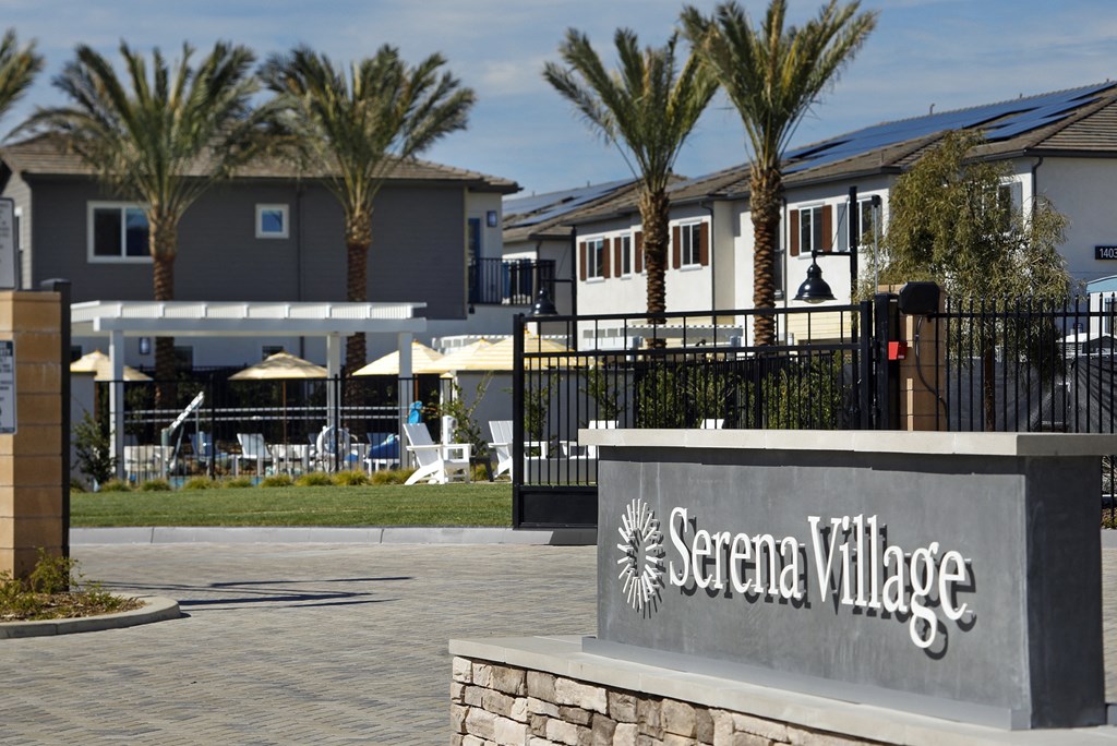 The image shows the entrance to Serena Village with a sign and palm trees in the background.