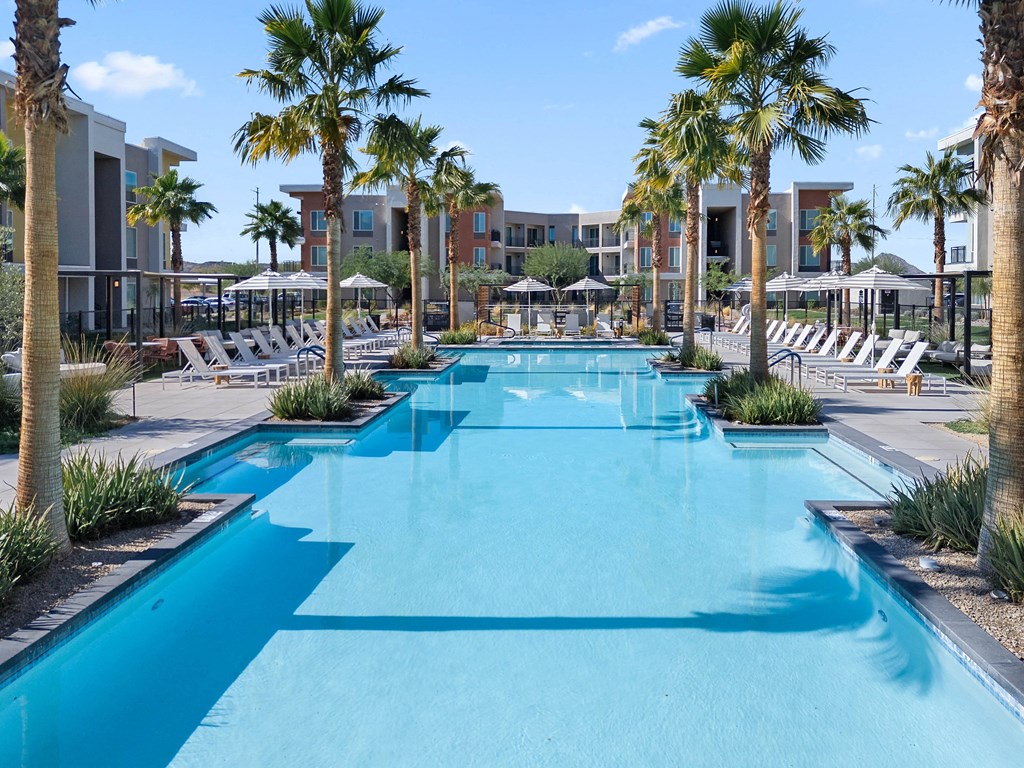 A long rectangular pool surrounded by palm trees and lounge chairs.