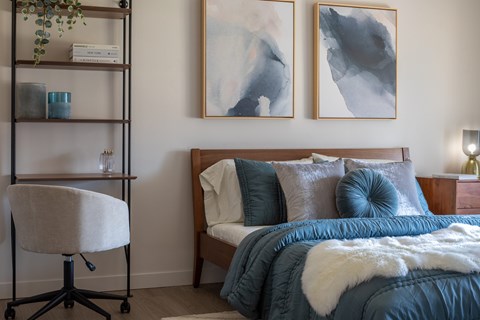 A bedroom with a bed, chair, and two paintings on the wall.