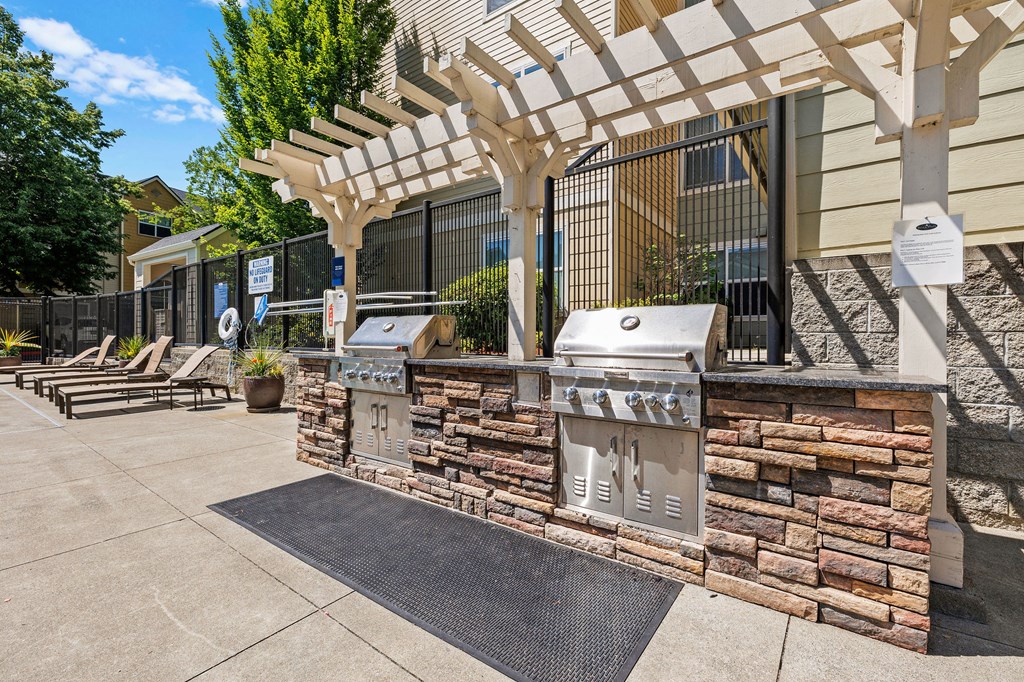 an outdoor barbecue area with two bbq grills and a pergola