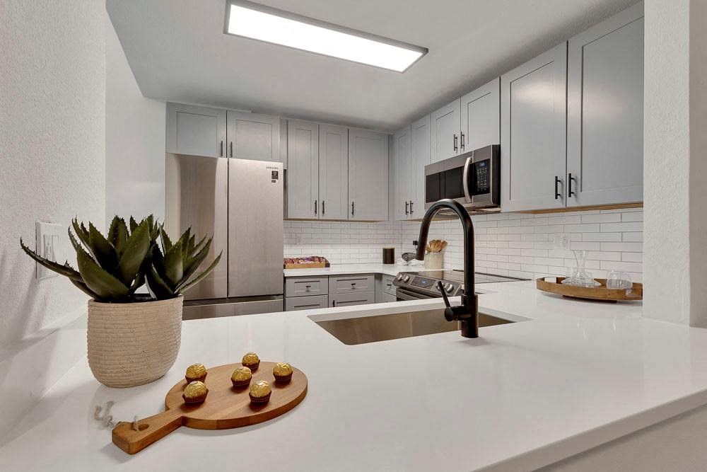 A kitchen with a white countertop and a wooden cutting board with food on it.