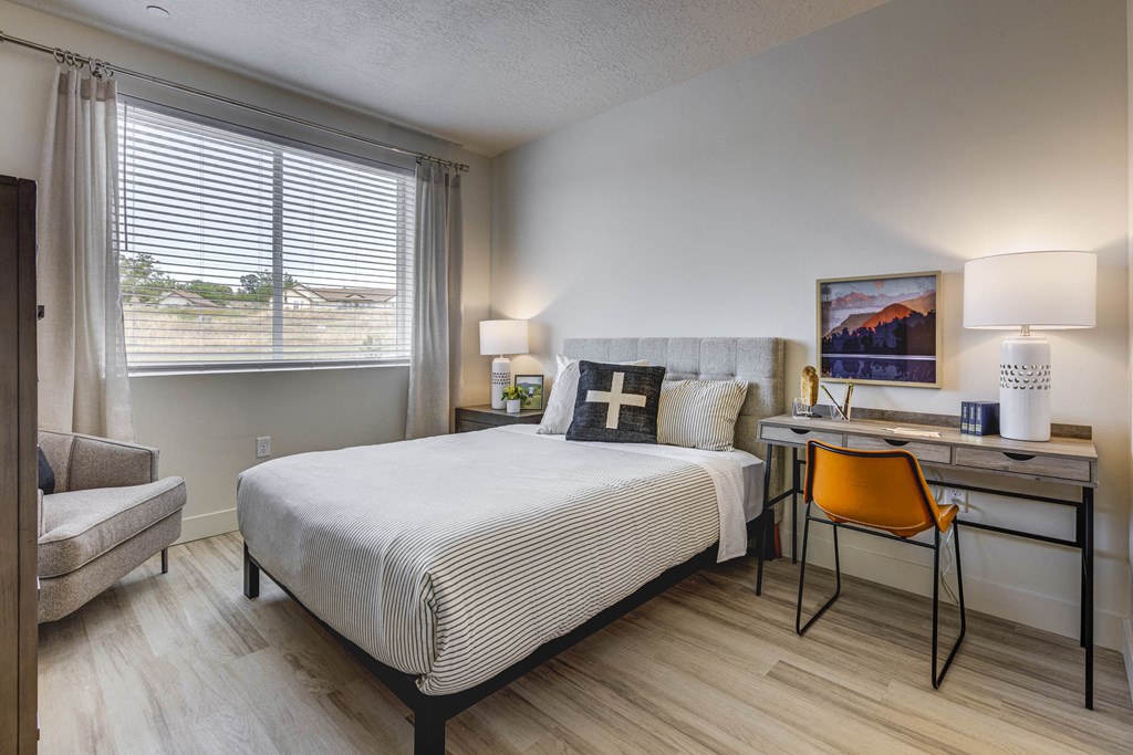 bedroom with decorated furnishings, wood tone floor, desk and window