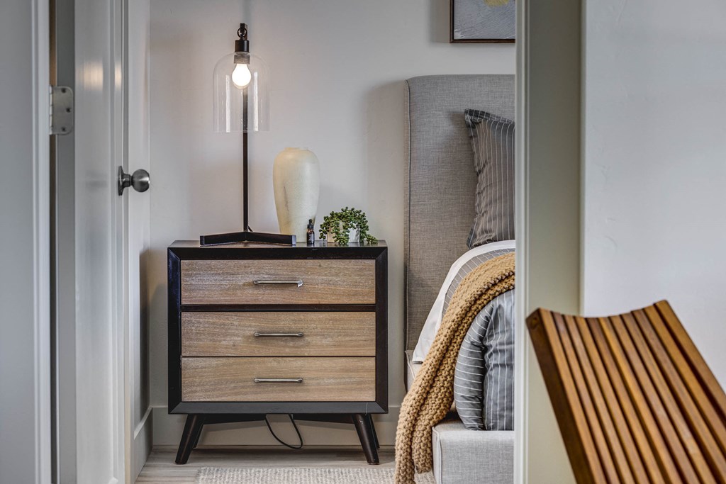 Close up of wood tone night stand, small plant, vase, and lamp through a  doorway