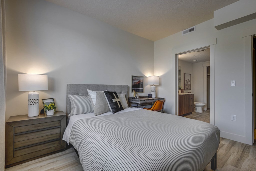 Bedroom with open door into en-suite bathroom, wood-tone floors, and décor