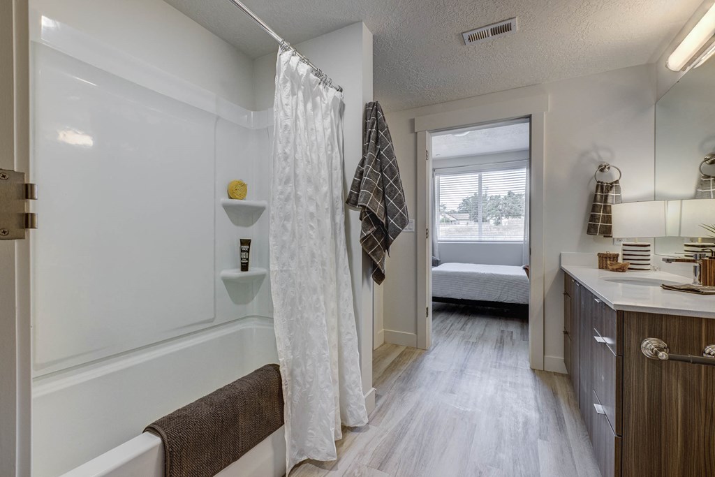 Bathroom with garden tub, wood tone floor, and open door leading to attached bedroom