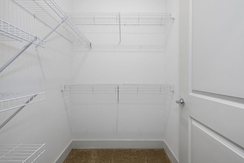 a walk in closet with white walls and shelves and a window