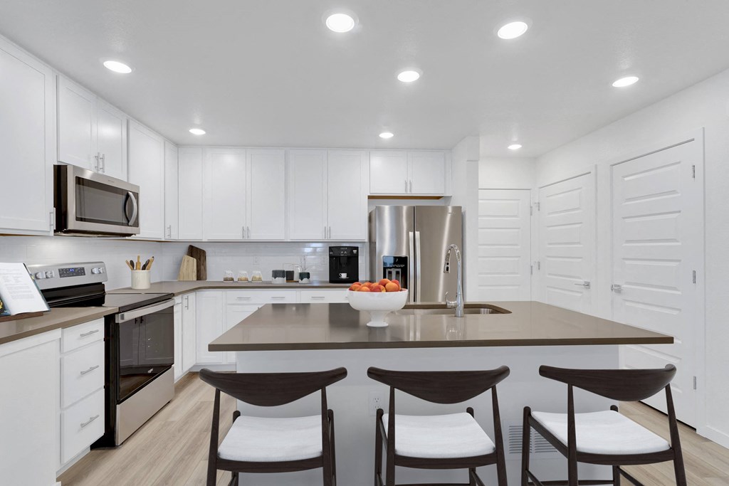 a kitchen with white cabinets and a large island with three chairs
