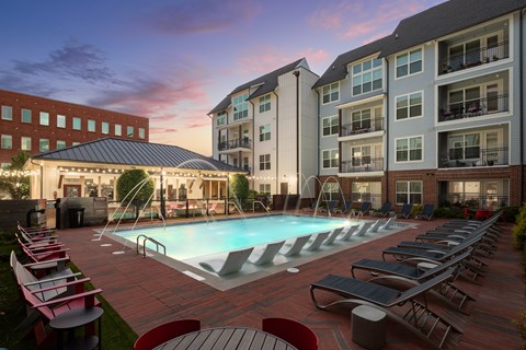 A swimming pool surrounded by lounge chairs and umbrellas in front of a building.