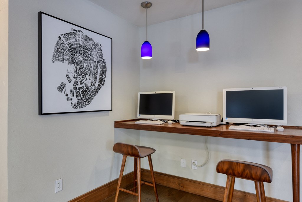 two computer monitors on a wooden desk with two stools