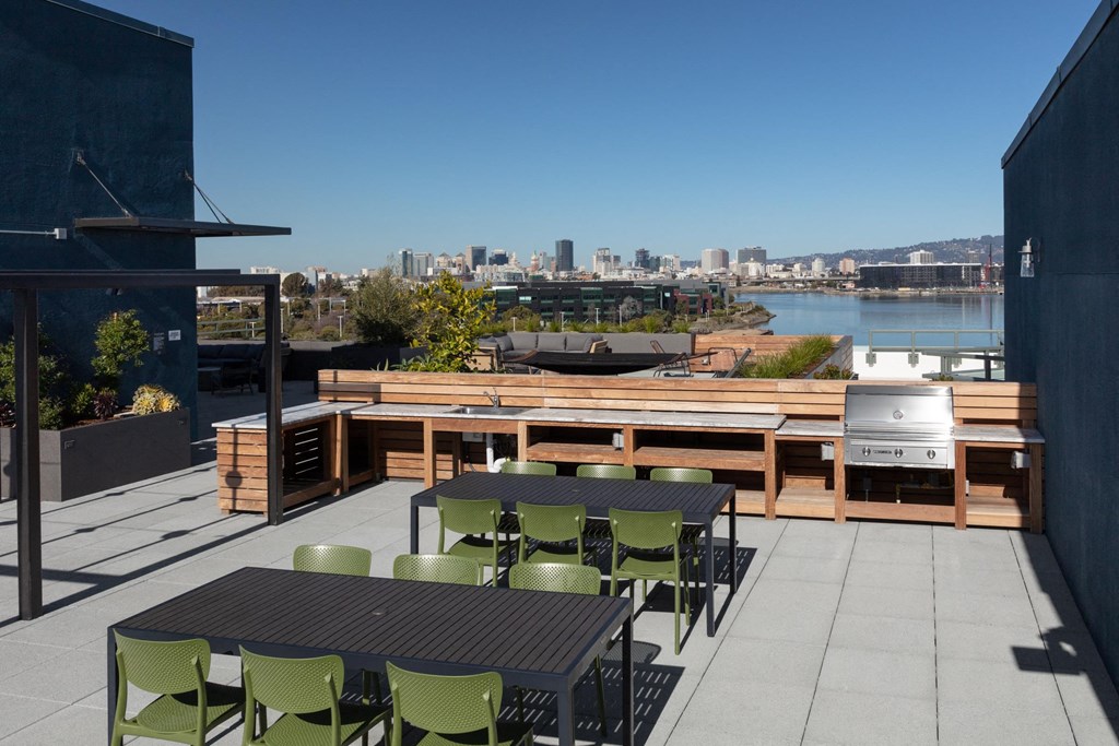 a rooftop patio with tables and chairs and a grill and a city in the background