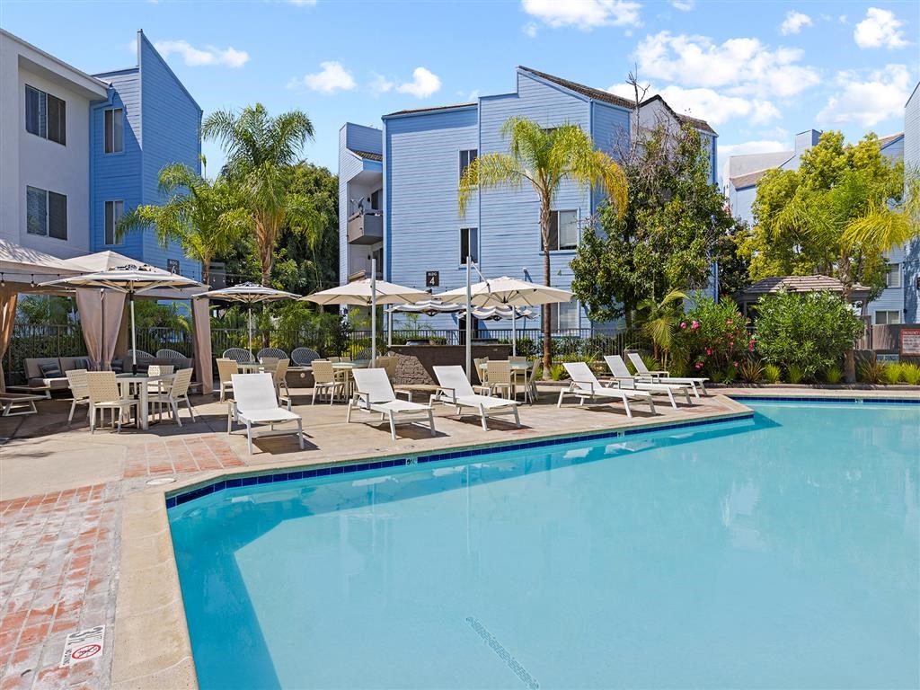 a swimming pool with lounge chairs and umbrellas in front of a building at Enclave, Paramount California