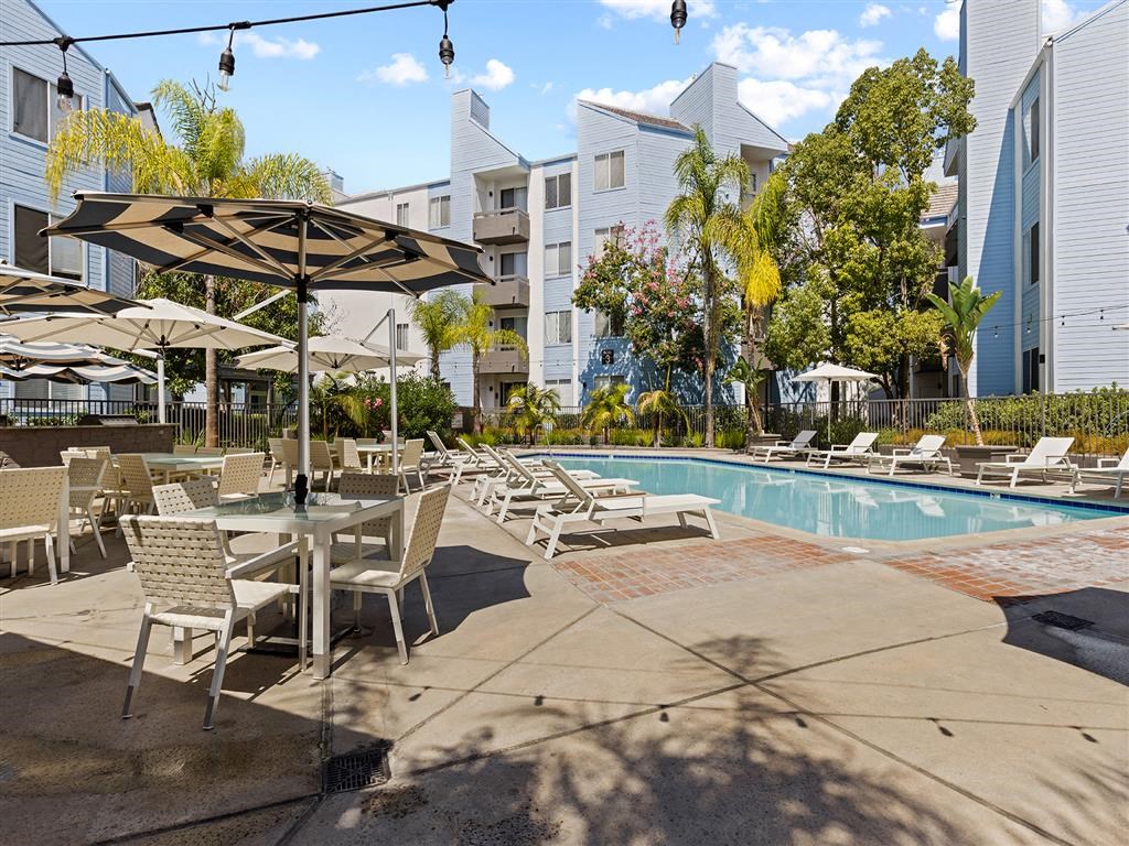 a swimming pool with tables and umbrellas and buildings in the background at Enclave, Paramount, CA 90723