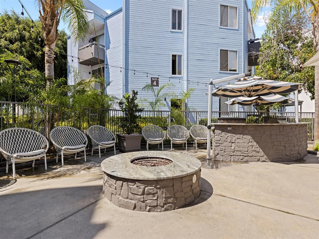 a fire pit with chairs and umbrellas in front of a white building at Enclave, Paramount California